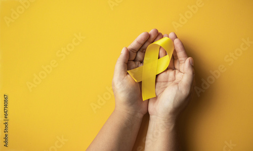 yellow ribbon on the hand of a cancer sick person, world cancer day, healthcare and medicine backdrop, suicide prevention, children health care.