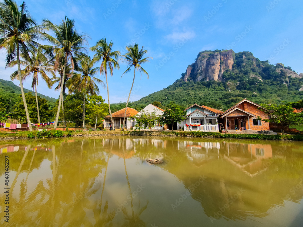 Fototapeta premium House in the countryside near the river with a mountain on background under the blue sky. Beautiful view of the village