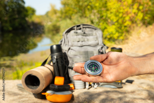 Man traveler holding a compass in her hand in the summer mountains at dawn.Tourist in the mountains with a compass against the backdrop of nature.The concept of tourism,sports and active recreation