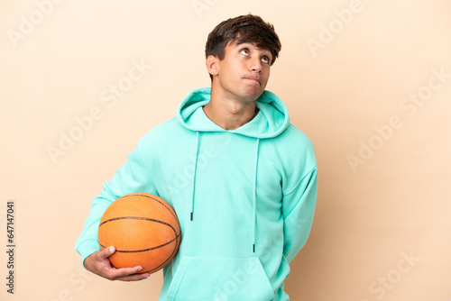 Handsome young basketball player man isolated on ocher background and looking up