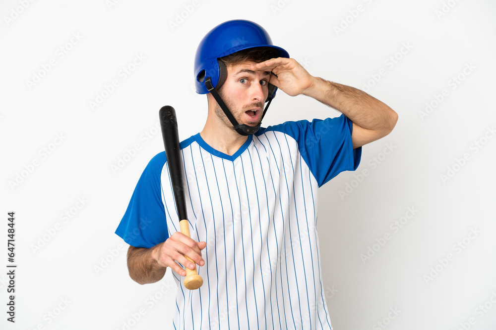 Young caucasian man playing baseball isolated on white background doing surprise gesture while looking to the side Young caucasian man playing baseball isolated on white background doing surprise gesture while looking to the side