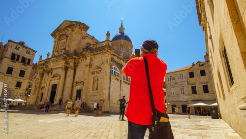 a tourist takes pictures of a church in the old town, while other tourists stroll down the street and enjoy the medieval architecture © soleg