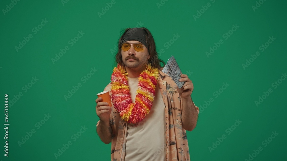 Stylish man traveller in casual clothing holding fan of money and paper cup, chilling at the party. Isolated on green background.