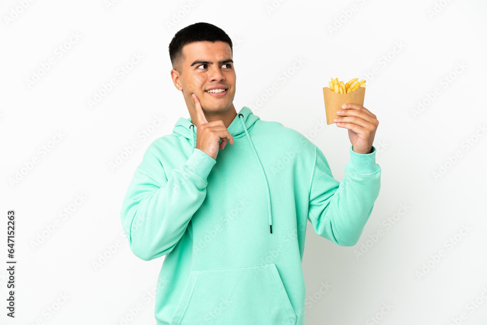 Young handsome man holding fried chips over isolated white background thinking an idea while looking up Young handsome man holding fried chips over isolated white background thinking an idea while looking up