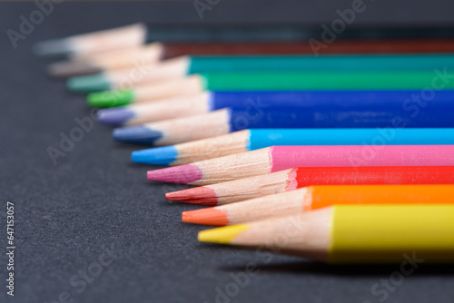 Collection set of colored pencils crayons orderly aligned in a row, art or drawing equipment on dark background.