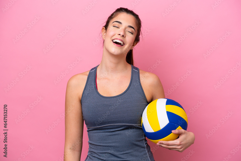 Young Brazilian woman playing volleyball isolated on pink background laughing