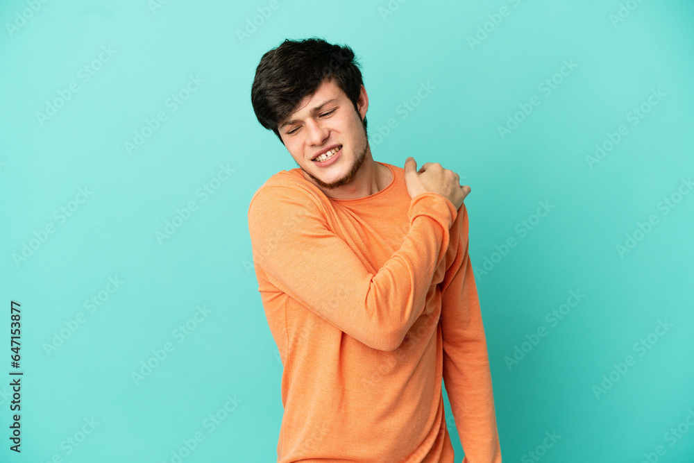 Young Russian man isolated on blue background suffering from pain in shoulder for having made an effort Young Russian man isolated on blue background suffering from pain in shoulder for having made an effort