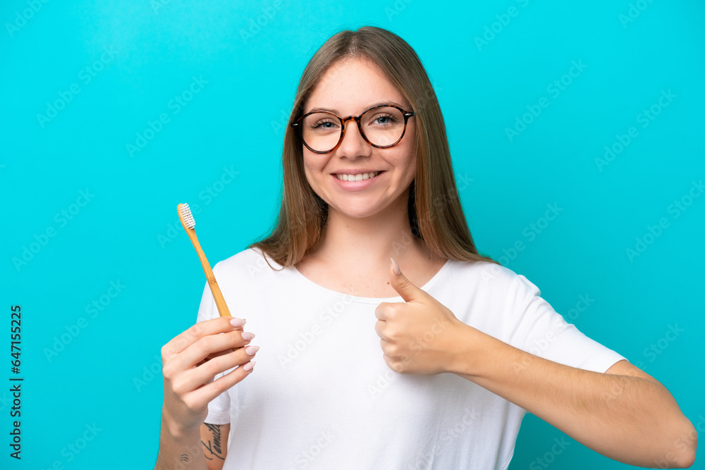 Young Lithuanian woman brushing teeth over isolated background with thumbs up because something good has happened Young Lithuanian woman brushing teeth over isolated background with thumbs up because something good has happened