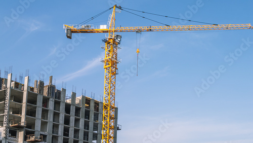 Construction of multi-apartment high-rise buildings in the city. Equipment for the construction and lifting of bulky loads during the construction of buildings. The tower crane lifts the load.