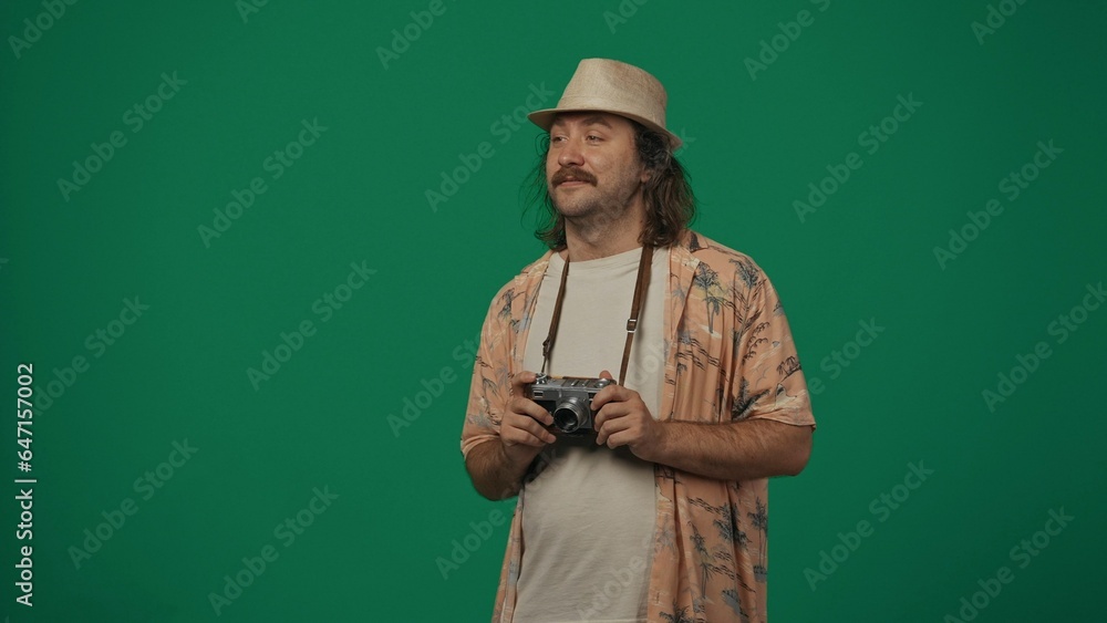 Man traveller in casual clothing and straw hat holding old film camera and looking away from the camera. Isolated on green background. Man traveller in casual clothing and straw hat holding old film camera and looking away from the camera. Isolated on green background.