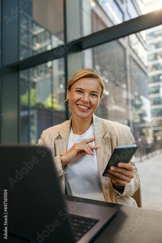 Stylish business woman use phone while sitting in modern coworking and working on laptop