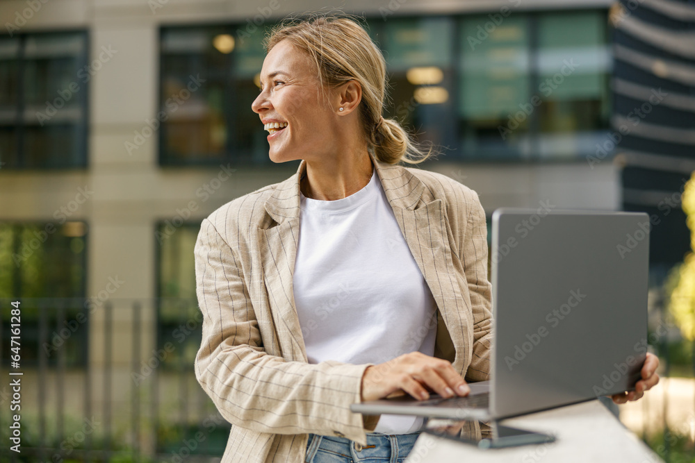 Stylish smiling woman entrepreneur working on laptop outside on modern building background Stylish smiling woman entrepreneur working on laptop outside on modern building background
