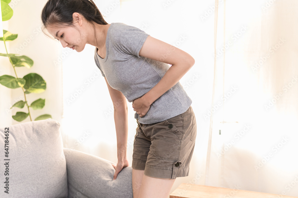 Fototapeta premium Healthcare medical or daily life concept : Young Asian woman holding stomach have a stomachache or menstruation pain sitting on her sofa.