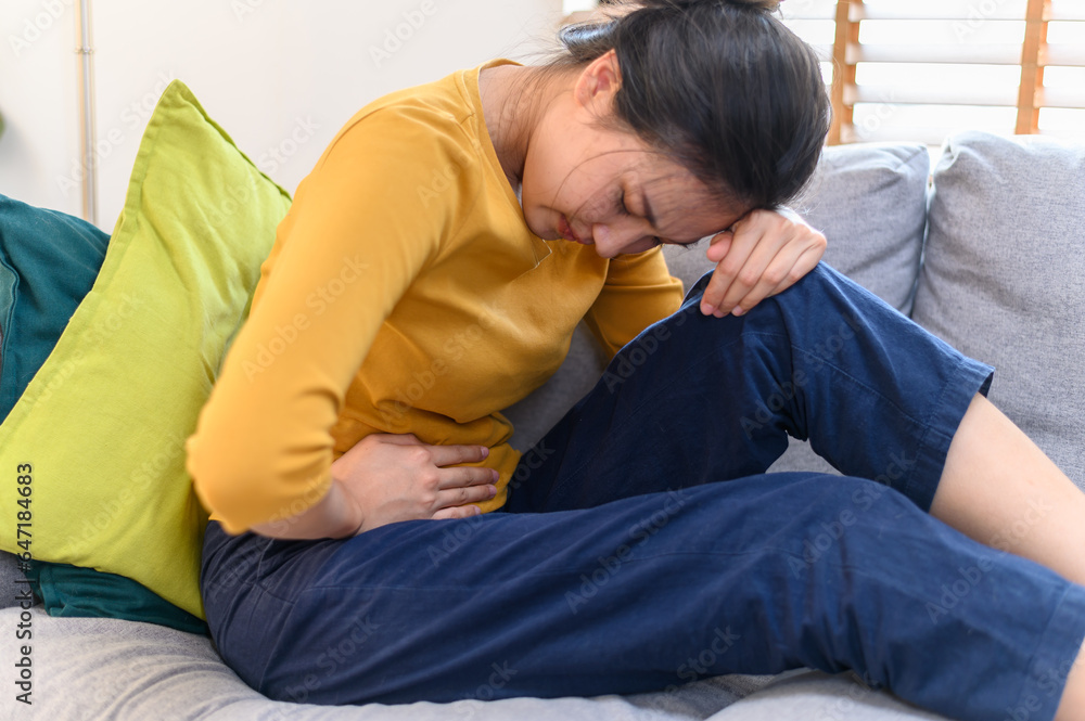 Healthcare medical or daily life concept : Close up stomach of young lady have a stomachache or menstruation pain sitting on a sofa. Young woman health daily lifestyle concept. Healthcare medical or daily life concept : Close up stomach of young lady have a stomachache or menstruation pain sitting on a sofa. Young woman health daily lifestyle concept.