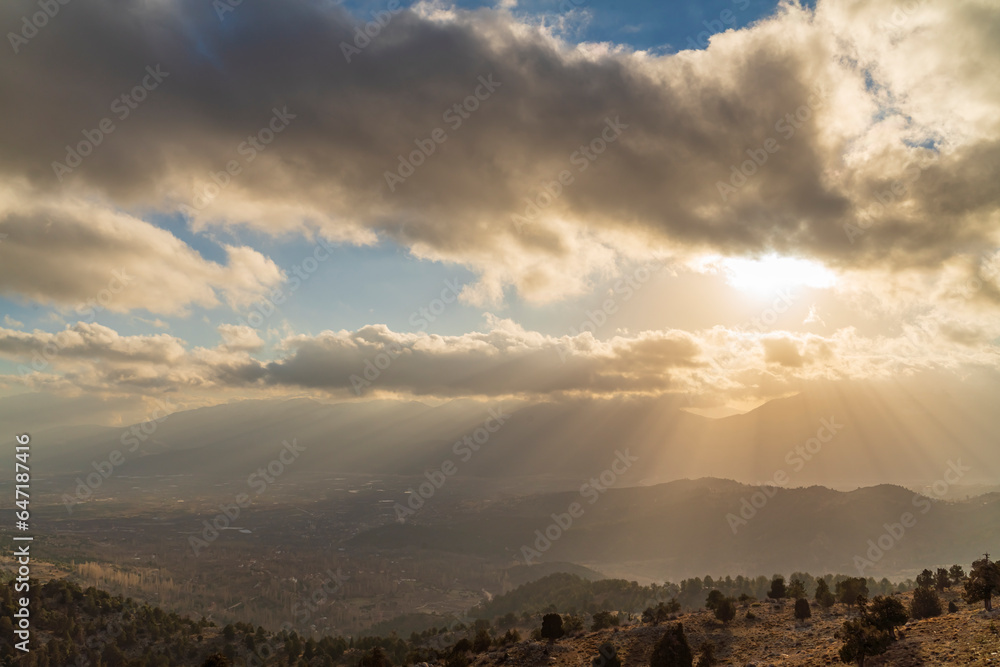 The sun rising behind the mountains and the rays of light leaking through the clouds