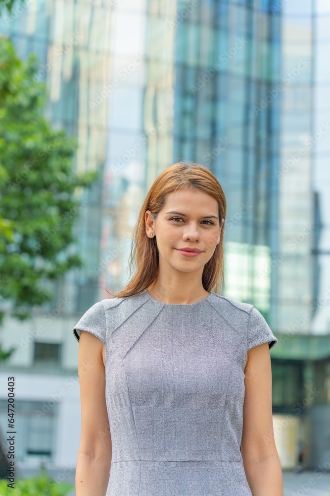Portrait of a young and successful white caucasian business woman standing in front of a modern cityscape of office buildings. Portrait of a young and successful white caucasian business woman standing in front of a modern cityscape of office buildings.