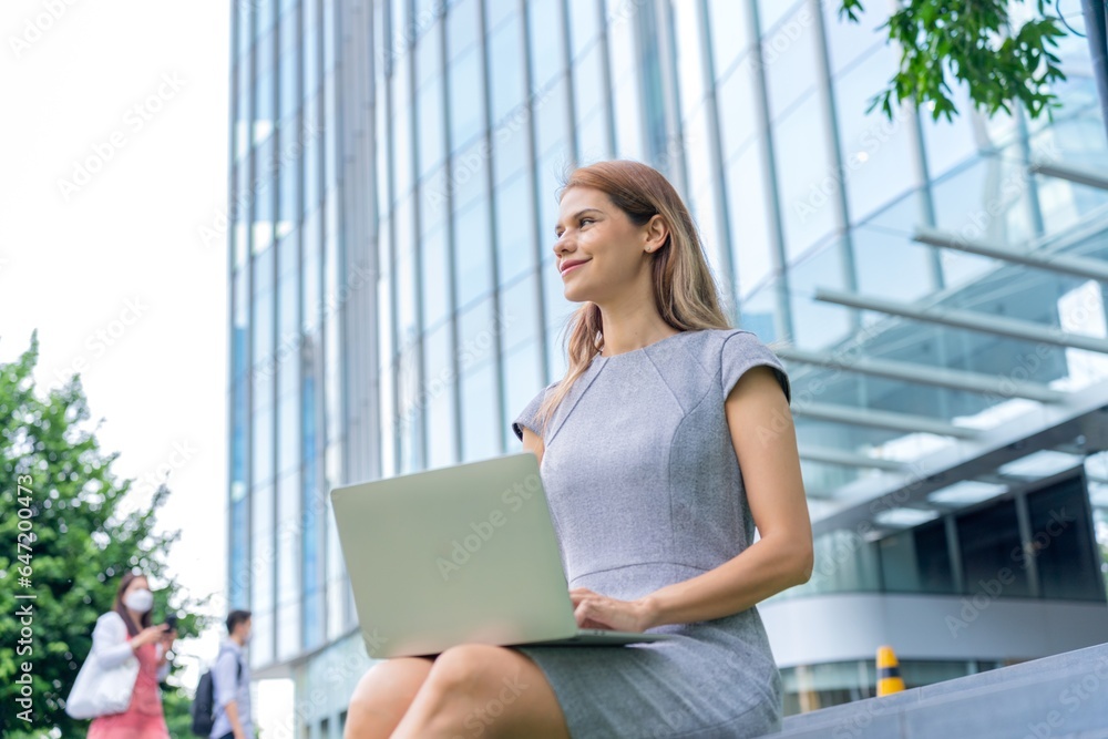 Fototapeta premium Young caucasian businesswoman working remotely outside her office building