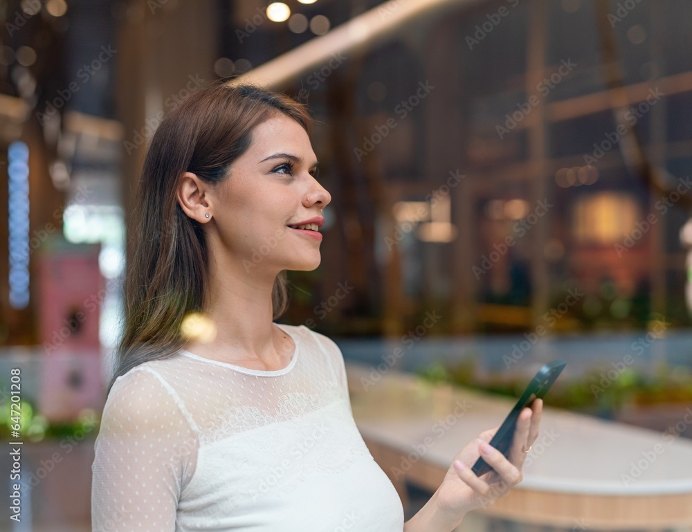 Young woman using smartphone behind the glass of a cafe