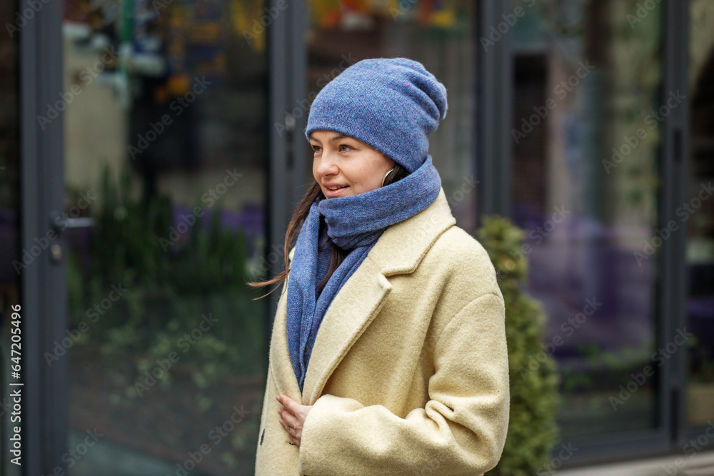 Smiling woman wearing stylish coat in city. Blue knitted hat and scarf. Happy mood. Smiling woman wearing stylish coat in city. Blue knitted hat and scarf. Happy mood.