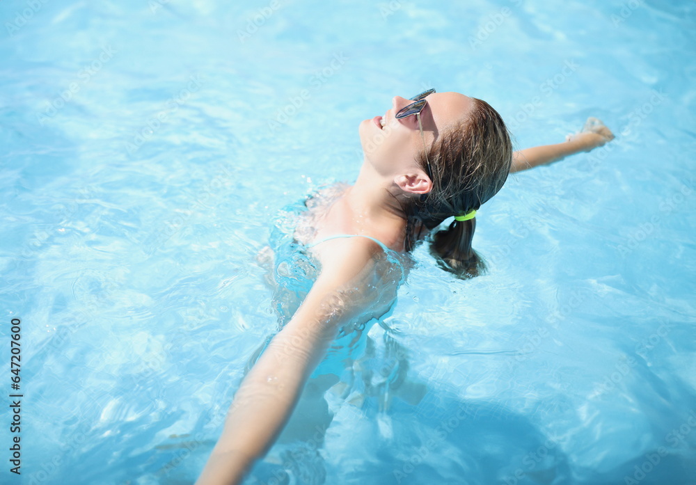 Portrait of happy young woman swim in pool, enjoy sun, sunbathe in water, relaxing atmosphere on vacation, sunny day. Holiday, resort, hotel, fun concept
