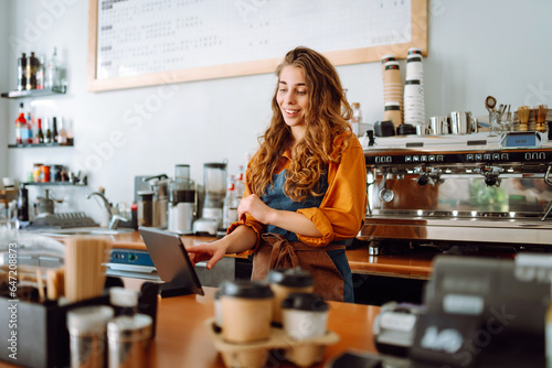 Smiling female barista takes an order from a panchette while standing at the bar counter in a coffee shop. Business concept. The concept of tenologies, takeaway food.