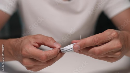 Closeup cropped shot of unrecognizable man unpacking new charging lightning cable during unboxing new smartphone sitting on white table background, close-up, front view. Shooting in slow motion.