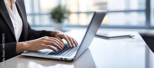 An image featuring a businesswoman's hands as she types on a sleek laptop computer keyboard at a modern office desk photo