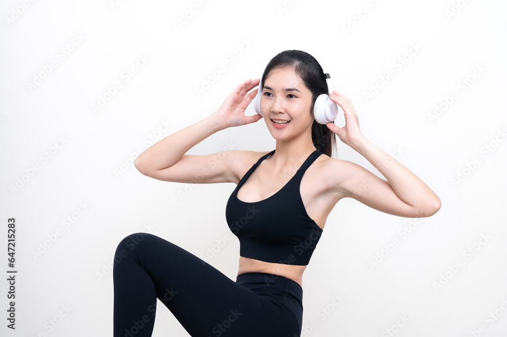 Happy slim asian woman in black workout clothes listening to music through headphones while exercising isolated with white background Happy slim asian woman in black workout clothes listening to music through headphones while exercising isolated with white background