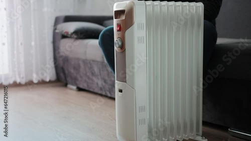 A man in warm socks sits in an apartment and warms himself from an electric heater. The concept of heating in an apartment in winter. Copy space for text photo