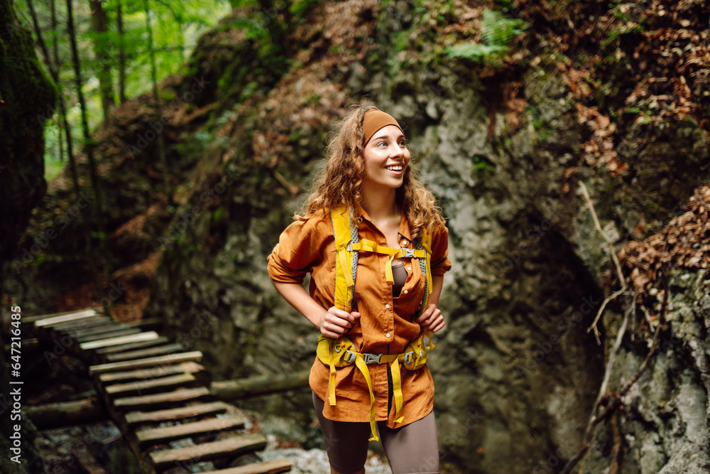 Happy woman in hiking clothes with a yellow backpack walks along a wooden hiking path in the mountains. Hiking, active lifestyle. Outdoor adventure concept. Happy woman in hiking clothes with a yellow backpack walks along a wooden hiking path in the mountains. Hiking, active lifestyle. Outdoor adventure concept.