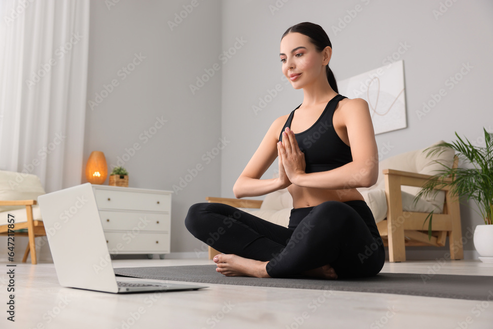 Beautiful young woman practicing Padmasana while watching online class on yoga mat at home, low angle view. Lotus pose Beautiful young woman practicing Padmasana while watching online class on yoga mat at home, low angle view. Lotus pose