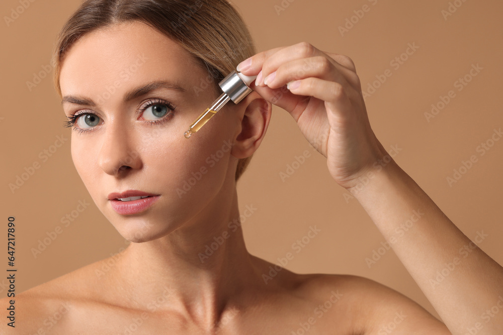 Beautiful woman applying cosmetic serum onto her face on beige background, closeup Beautiful woman applying cosmetic serum onto her face on beige background, closeup