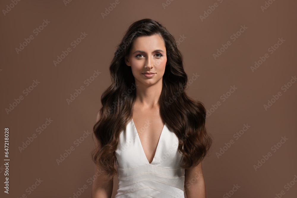 Hair styling. Portrait of beautiful woman with wavy long hair on brown background Hair styling. Portrait of beautiful woman with wavy long hair on brown background
