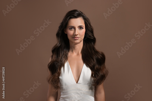 Hair styling. Portrait of beautiful woman with wavy long hair on brown background
