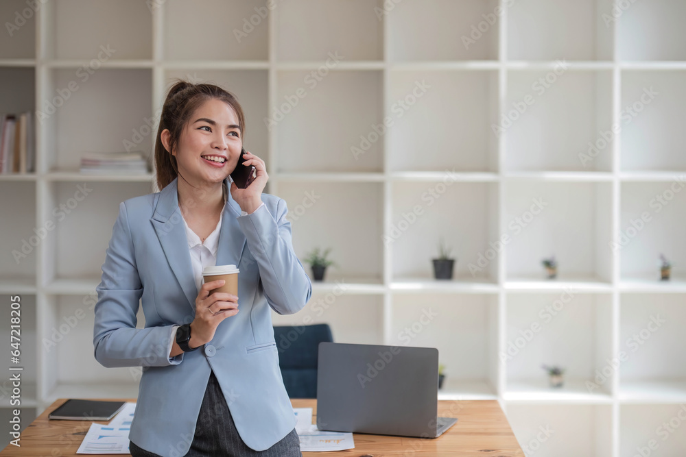 Asian businesswoman using mobile phone Smiling and happy while standing at desk in modern office Asian businesswoman using mobile phone Smiling and happy while standing at desk in modern office