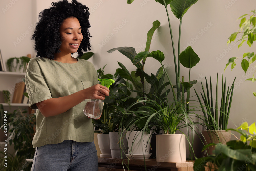 Happy woman spraying beautiful houseplants with water indoors Happy woman spraying beautiful houseplants with water indoors
