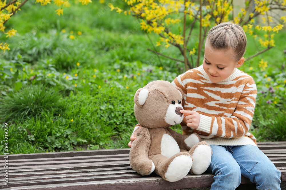 Little girl with teddy bear on wooden bench outdoors. Space for text Little girl with teddy bear on wooden bench outdoors. Space for text