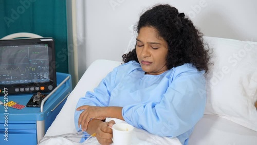 A middle-aged Indian woman sipping tea / coffee in a hospital room - hospital care  hospital food  ecg monitor. Asian female patient in blue hospital dress - hospital bed  sick lady  medical proble... photo