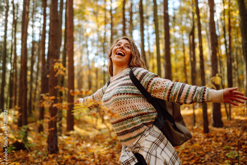 Tourist with a hiking backpack, hat walks along a path in the autumn forest. Beautiful woman enjoys a sunny day in nature, feels freedom and breathes fresh air, explores nature. photo