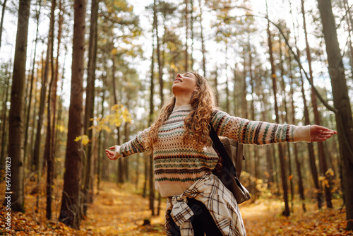 Fototapeta Tourist with a hiking backpack, hat walks along a path in the autumn forest