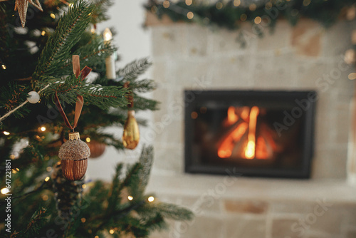 Stylish christmas gold acorn on tree close up against burning fireplace. Beautiful decorated christmas tree with vintage ornaments, ribbons and lights. Christmas background. Merry Christmas! photo