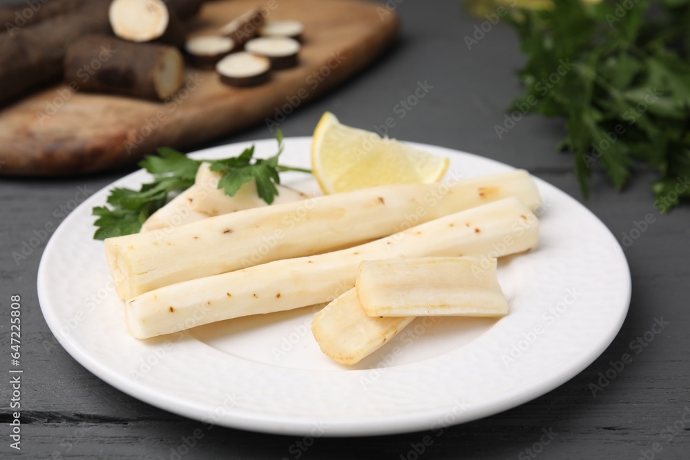 Cut raw salsify roots with parsley and lemon on grey wooden table, closeup