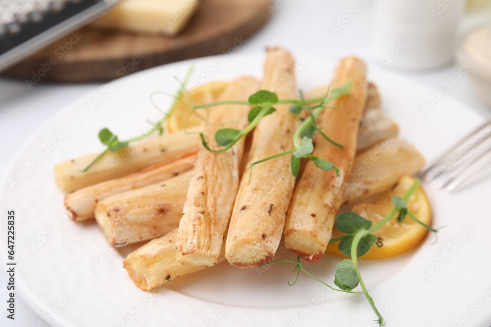Plate with baked salsify roots and lemon on table, closeup