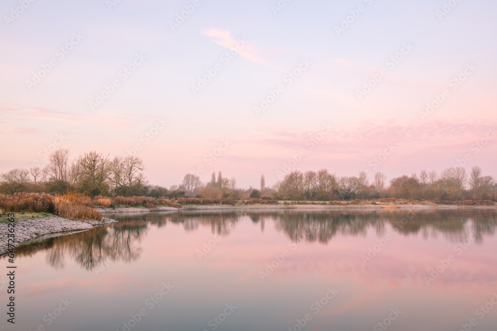 Winter sunrise at Tar Lakes in Oxfordshire, trees reflected in still waters.