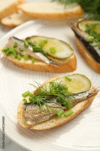 Delicious sandwiches with sprats, pickled cucumber, green onion and dill on plate, closeup