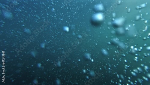Slow motion footage showcasing air bubbles gracefully ascending from the ocean floor to the water's surface, with a diver releasing bubbles. Ideal for an abstract and serene natural background.
