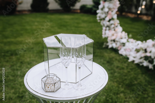 Wedding accessories, details: glass box, money box, wine glasses stand on the table, rack outdoors in the ceremony. Close-up photo.