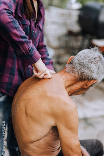 An adult woman, a professional doctor, makes a relaxing massage to a sick old elderly gray-haired retired man with scoliosis in the spine on his back. Photography, lifestyle.