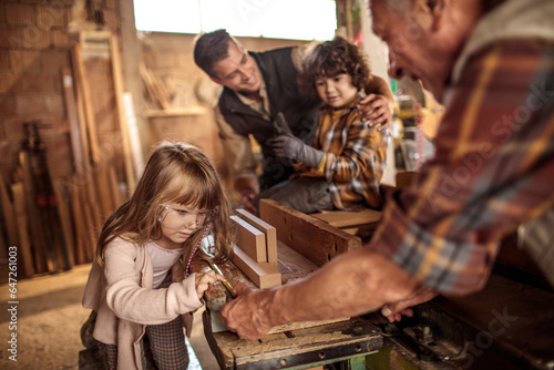 Grandfather carpenter teaching his son and grandchildren how to work with wood in a wood workshop © Geber86