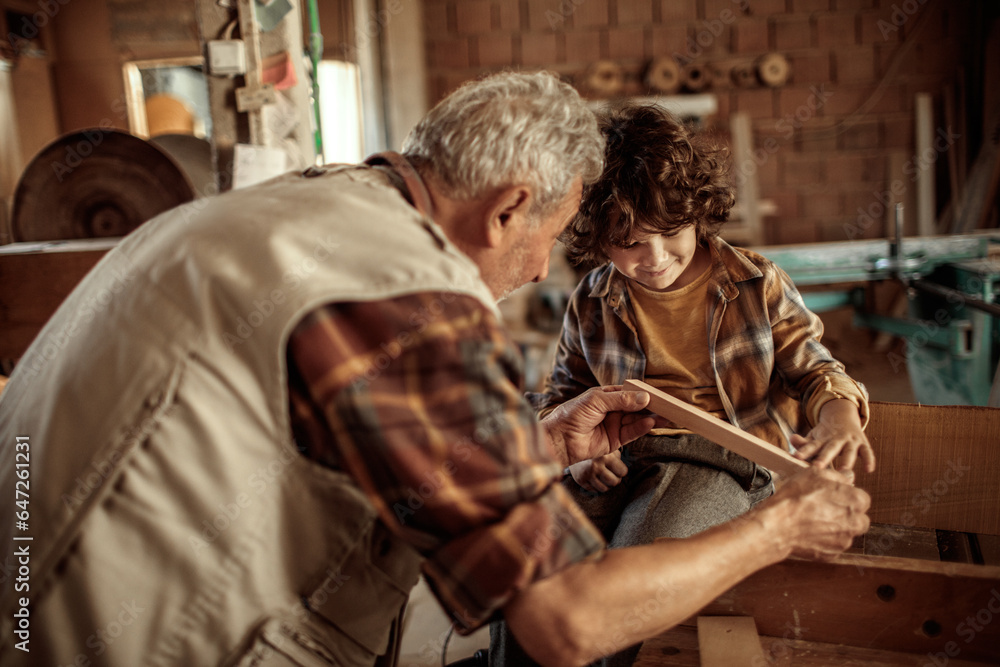 Grandfather carpenter teaching his grandson how to work with wood in a wood workshop